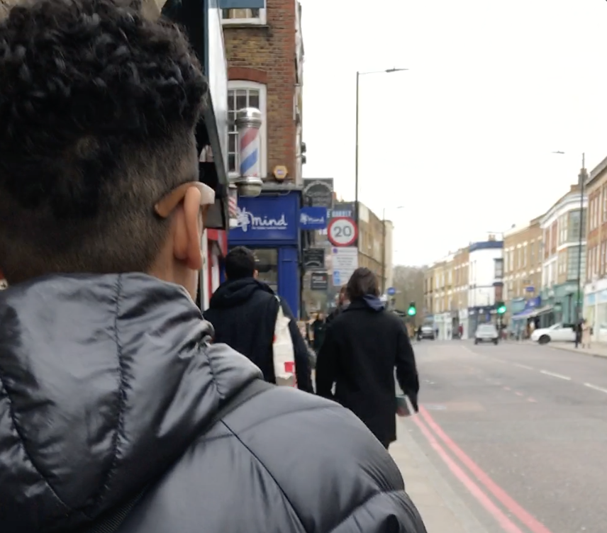 Photo of P1 as they walk down a street with signage in the background